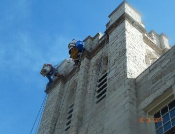 Steeplejack performing tuck pointing and stone restoration on church bell tower
